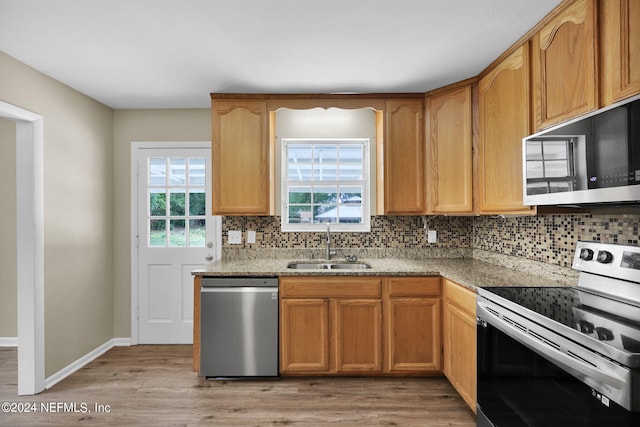 kitchen featuring backsplash, light hardwood / wood-style floors, sink, light stone countertops, and appliances with stainless steel finishes