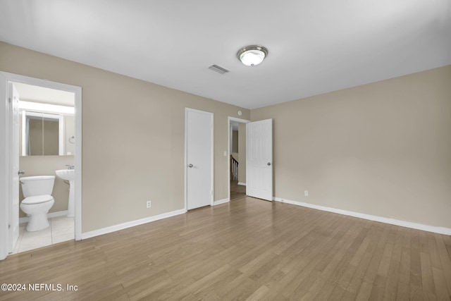 unfurnished bedroom featuring ensuite bathroom and light hardwood / wood-style flooring