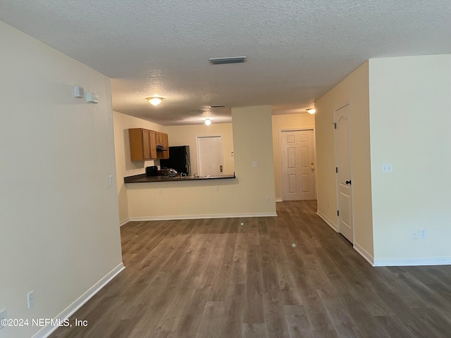 unfurnished living room featuring baseboards, visible vents, dark wood finished floors, and a textured ceiling