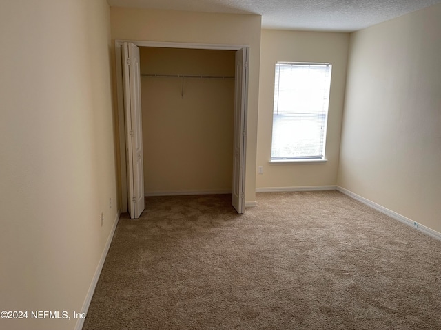 unfurnished bedroom with carpet, a closet, a textured ceiling, and baseboards