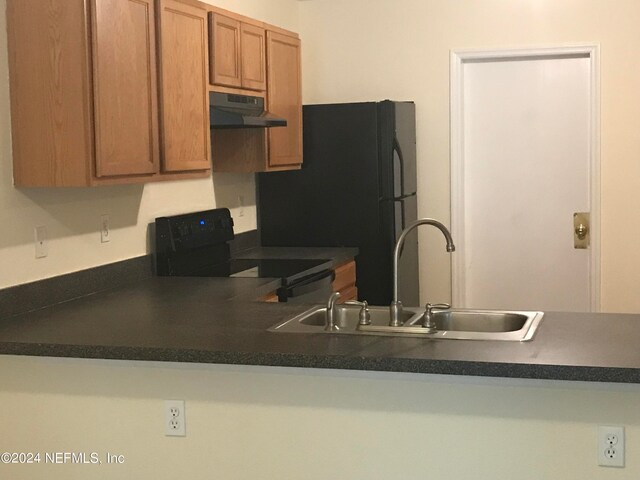 kitchen featuring brown cabinets, dark countertops, a sink, under cabinet range hood, and black appliances