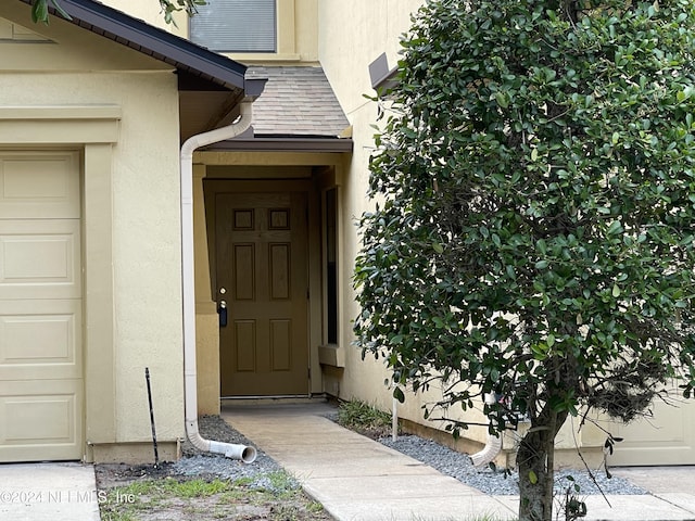 property entrance with a garage, roof with shingles, and stucco siding