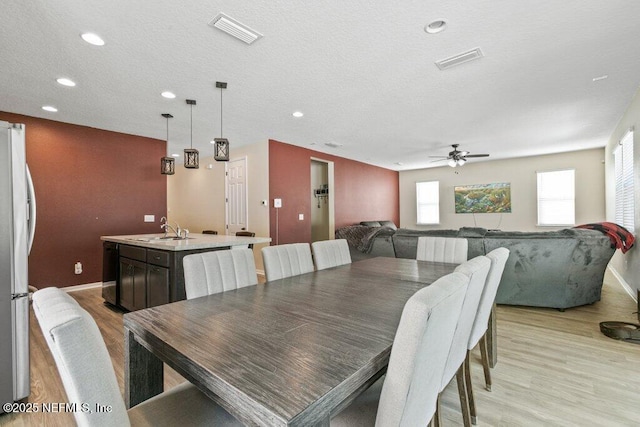 dining area with light wood-type flooring, a ceiling fan, baseboards, and visible vents