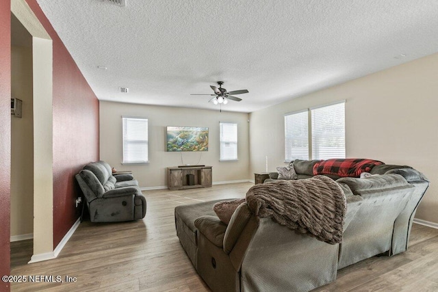 living area with a wealth of natural light, a ceiling fan, a textured ceiling, and light wood-type flooring