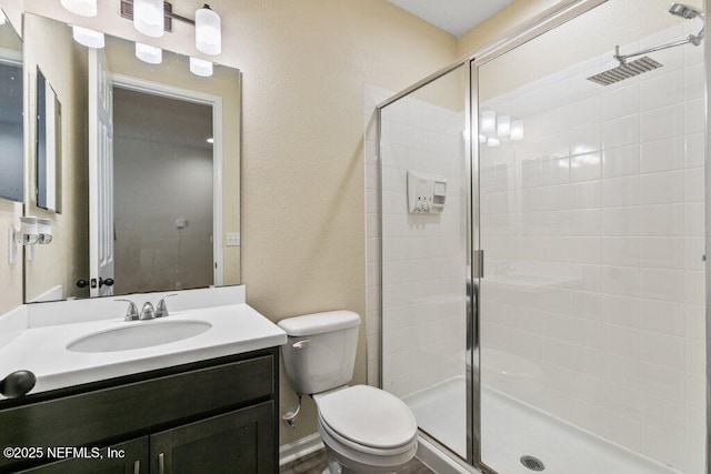 full bathroom featuring toilet, vanity, a textured wall, and a stall shower