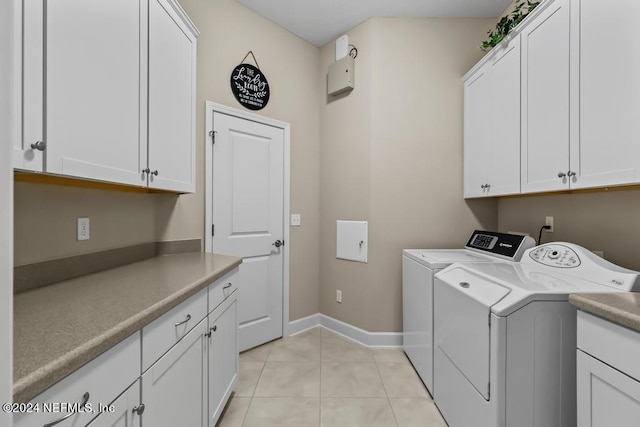 clothes washing area with cabinets, light tile floors, and washing machine and clothes dryer