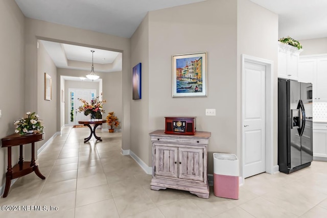 hallway with a tray ceiling and light tile floors