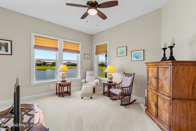 living area with light carpet, ceiling fan, and a water view