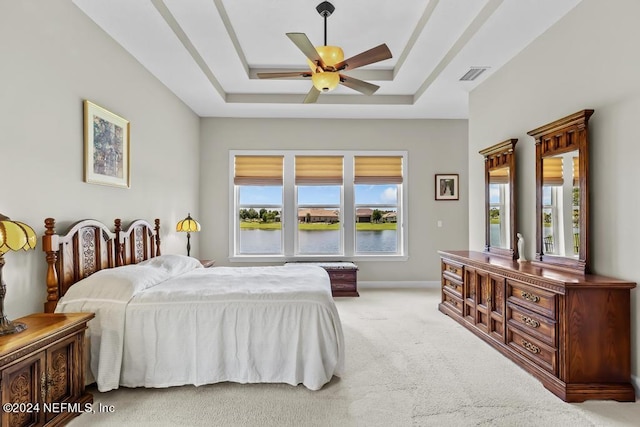 bedroom featuring carpet floors, ceiling fan, a water view, and a raised ceiling