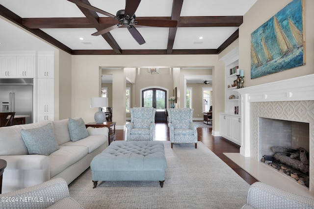 living room with dark hardwood / wood-style floors, a tiled fireplace, coffered ceiling, beam ceiling, and built in shelves