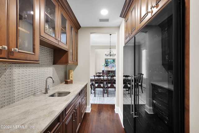 kitchen with dark wood-type flooring, sink, pendant lighting, light stone countertops, and backsplash