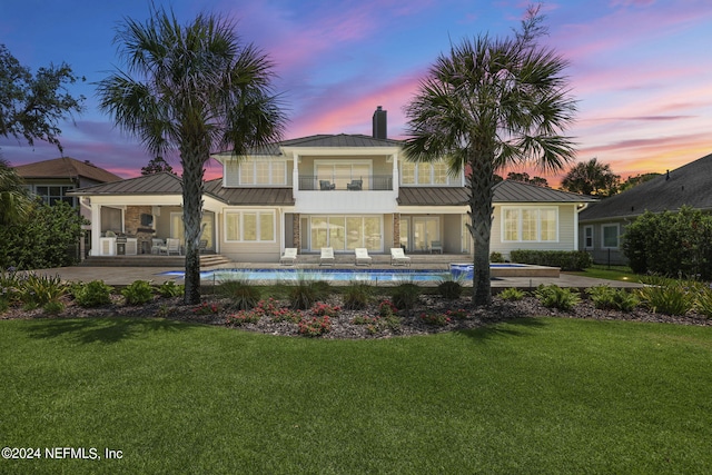 back house at dusk featuring a balcony, a yard, and a patio area