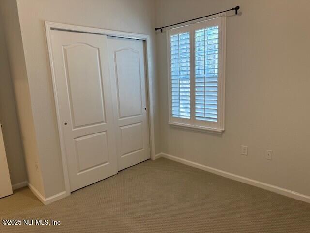 unfurnished bedroom with light carpet, multiple windows, a closet, and baseboards