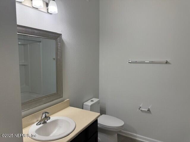 bathroom with toilet, baseboards, a shower, and vanity