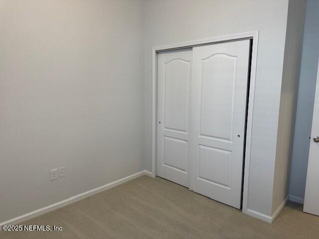 unfurnished bedroom with light carpet, baseboards, and a closet