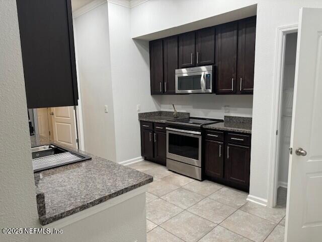 kitchen with baseboards, dark stone counters, stainless steel appliances, dark brown cabinets, and light tile patterned flooring