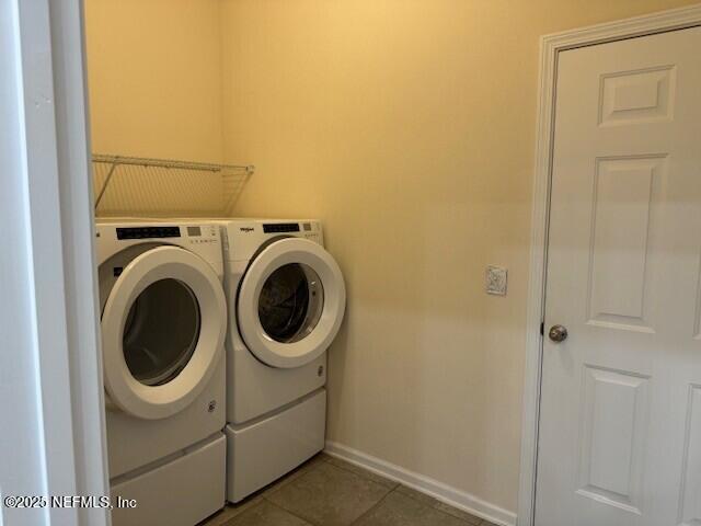 washroom featuring dark tile patterned flooring, laundry area, baseboards, and washing machine and clothes dryer