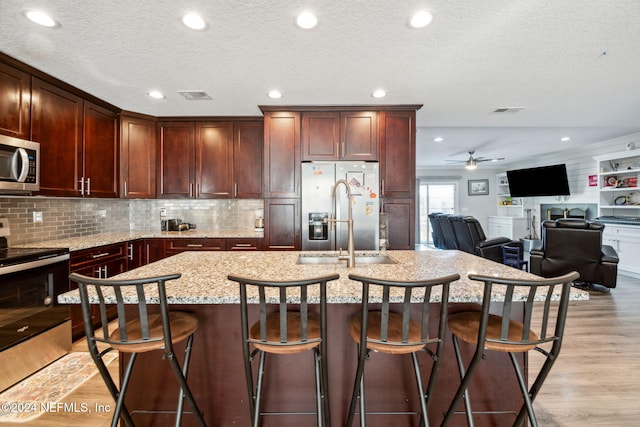 kitchen featuring light stone countertops, light wood-type flooring, an island with sink, stainless steel appliances, and a breakfast bar