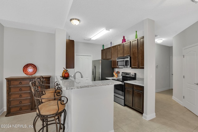 kitchen with light stone countertops, kitchen peninsula, light tile floors, a kitchen bar, and appliances with stainless steel finishes