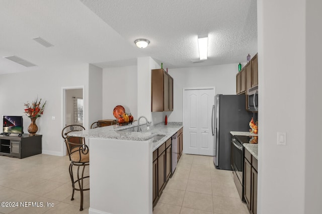 kitchen with light stone countertops, stainless steel appliances, light tile flooring, sink, and a kitchen bar