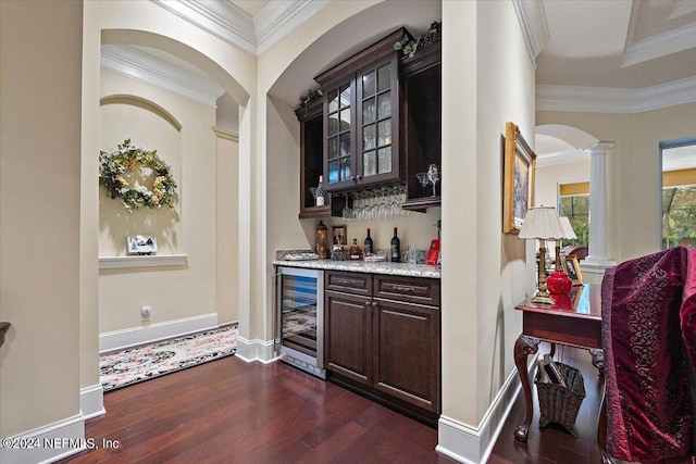 bar featuring dark brown cabinets, beverage cooler, decorative columns, dark hardwood / wood-style flooring, and ornamental molding