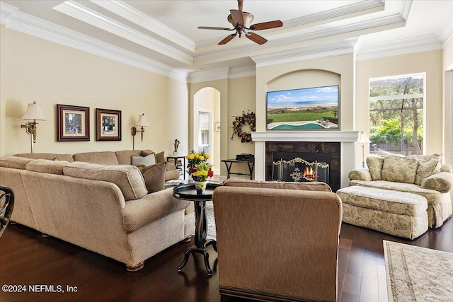 living room featuring a high end fireplace, ceiling fan, crown molding, dark wood-type flooring, and a raised ceiling