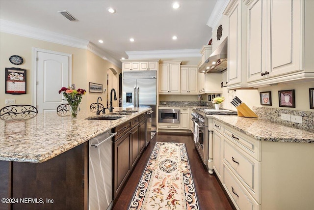 kitchen with built in appliances, dark wood-type flooring, light stone counters, wall chimney range hood, and sink