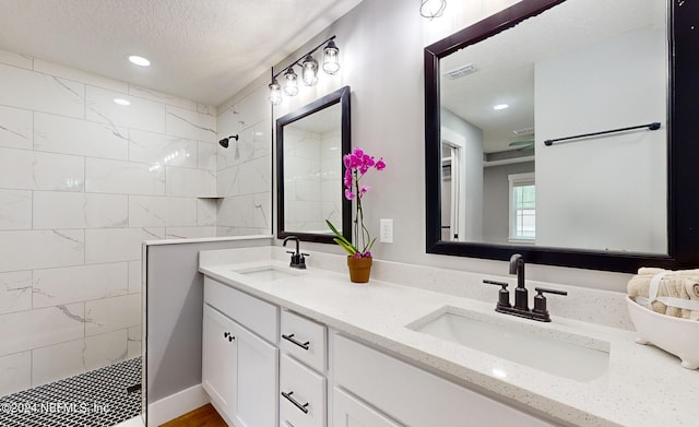 bathroom featuring tiled shower, double vanity, and a textured ceiling