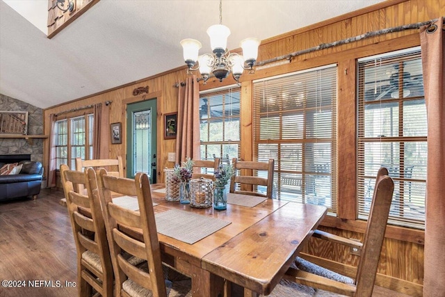 dining area with vaulted ceiling, an inviting chandelier, a fireplace, dark wood-type flooring, and wooden walls