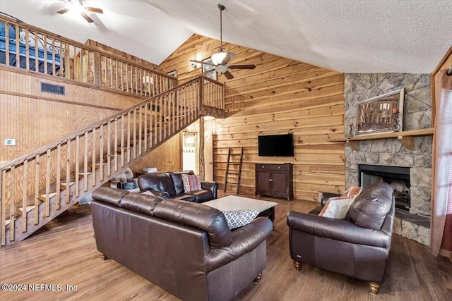 living room featuring a textured ceiling, wooden walls, hardwood / wood-style floors, a stone fireplace, and ceiling fan