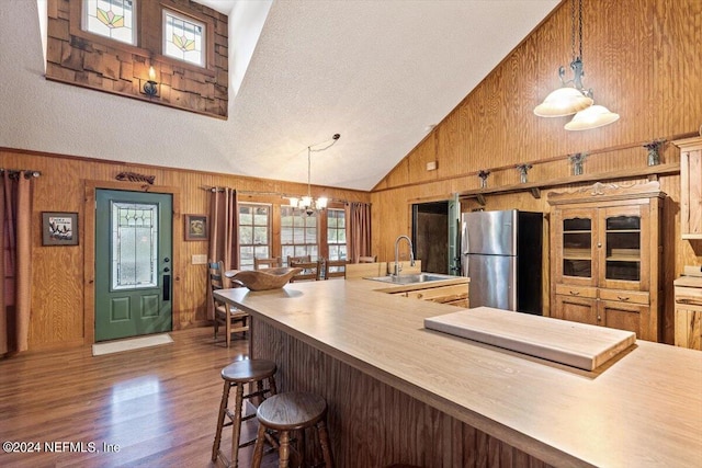 kitchen featuring stainless steel fridge, dark hardwood / wood-style flooring, high vaulted ceiling, sink, and wood walls