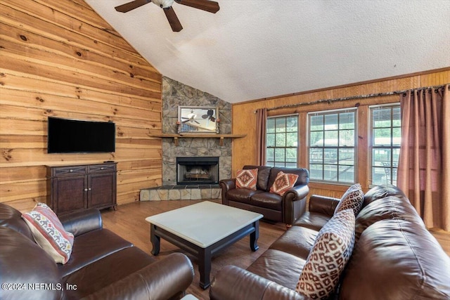 living room with a textured ceiling, lofted ceiling, hardwood / wood-style flooring, a stone fireplace, and ceiling fan