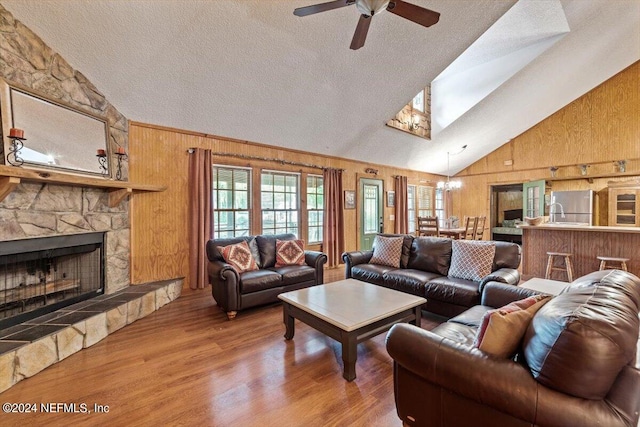 living room featuring vaulted ceiling, a fireplace, ceiling fan with notable chandelier, wood walls, and hardwood / wood-style flooring