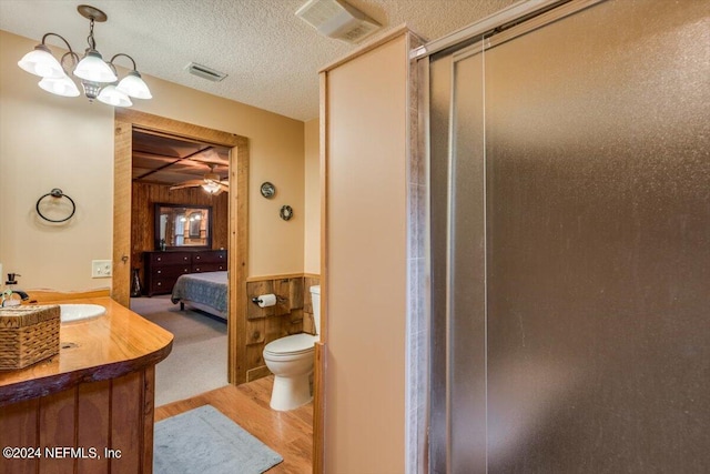 bathroom with a textured ceiling, ceiling fan with notable chandelier, hardwood / wood-style flooring, vanity, and toilet