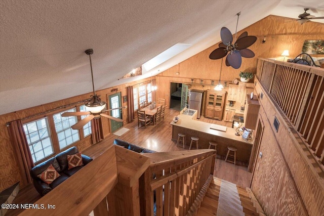 living room featuring ceiling fan, hardwood / wood-style floors, wood walls, and a skylight