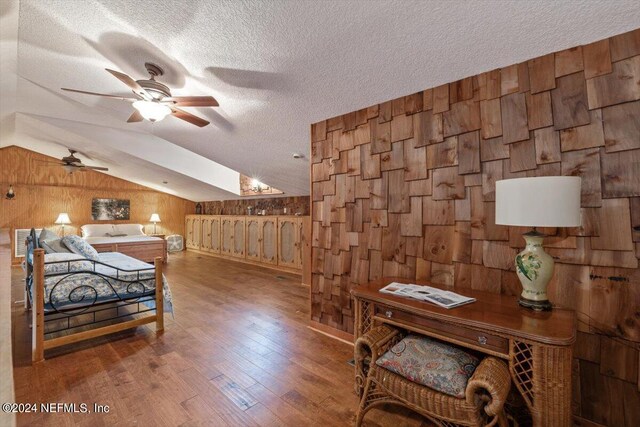 bedroom featuring wood walls, a textured ceiling, wood-type flooring, and vaulted ceiling