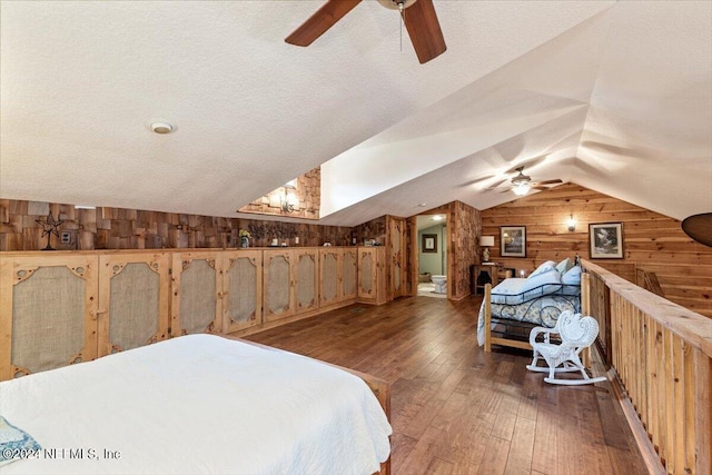 bedroom featuring a textured ceiling, dark hardwood / wood-style flooring, wood walls, ceiling fan, and vaulted ceiling