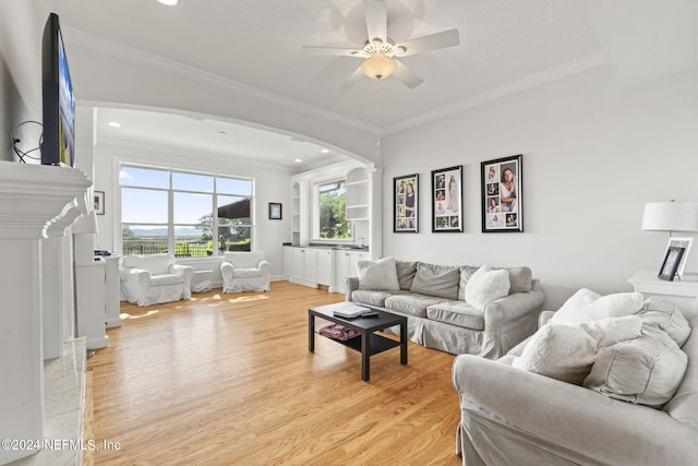 living room featuring a fireplace, light hardwood / wood-style flooring, ornamental molding, and ceiling fan