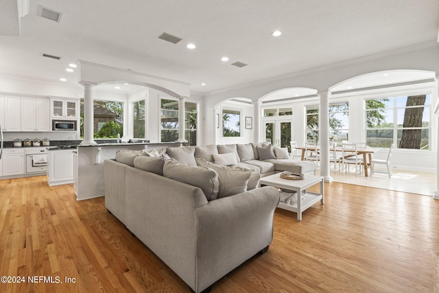 living room with decorative columns, ornamental molding, and light wood-type flooring