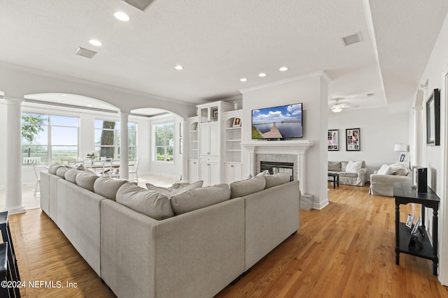 living room featuring a tile fireplace, decorative columns, crown molding, a textured ceiling, and light hardwood / wood-style flooring