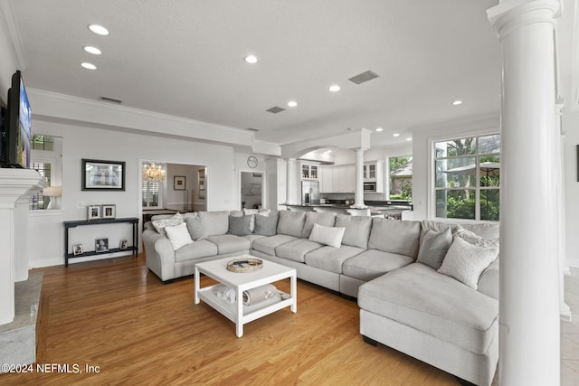 living room featuring a chandelier, ornamental molding, light hardwood / wood-style floors, and decorative columns