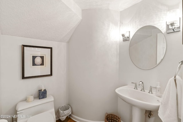 bathroom with sink, vaulted ceiling, toilet, and a textured ceiling