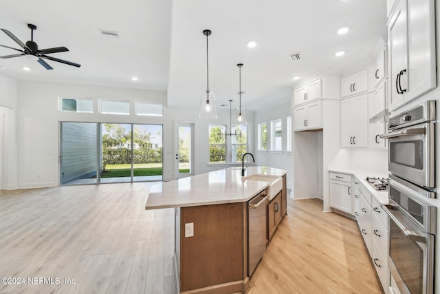 kitchen with white cabinetry, a center island with sink, decorative light fixtures, and light hardwood / wood-style flooring