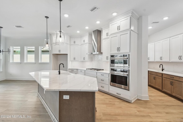 kitchen featuring light stone counters, sink, wall chimney range hood, white cabinets, and an island with sink