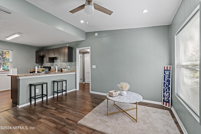 interior space with a kitchen breakfast bar, ceiling fan, sink, and dark wood-type flooring