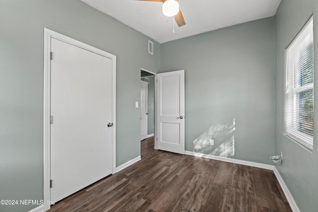 unfurnished bedroom featuring ceiling fan, dark hardwood / wood-style floors, a closet, and multiple windows