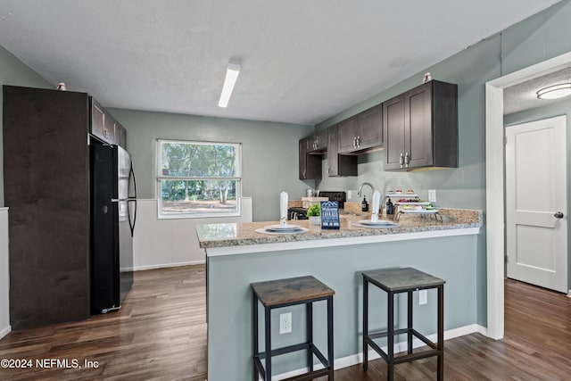 kitchen featuring a kitchen bar, black appliances, dark brown cabinets, dark hardwood / wood-style flooring, and kitchen peninsula