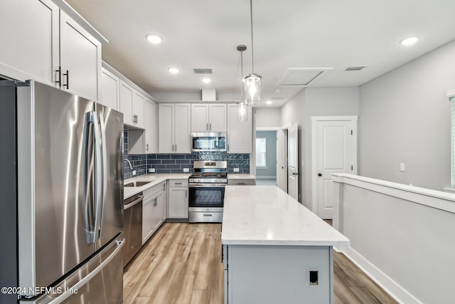 kitchen with a kitchen island, pendant lighting, sink, stainless steel appliances, and light stone countertops