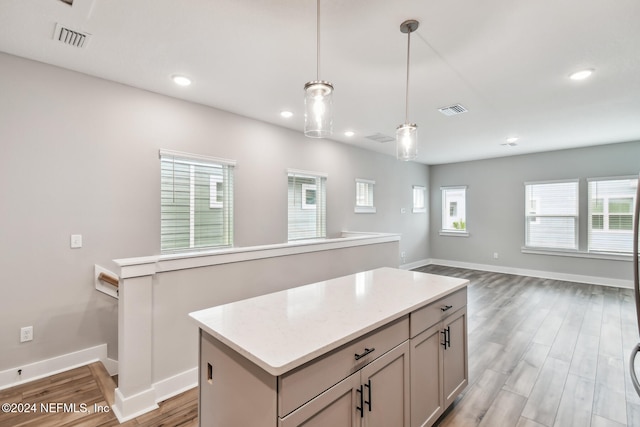 kitchen with hanging light fixtures, light stone countertops, a center island, and hardwood / wood-style floors