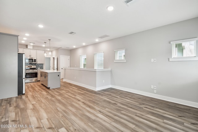 kitchen featuring light wood-type flooring, a kitchen island, pendant lighting, stainless steel appliances, and backsplash